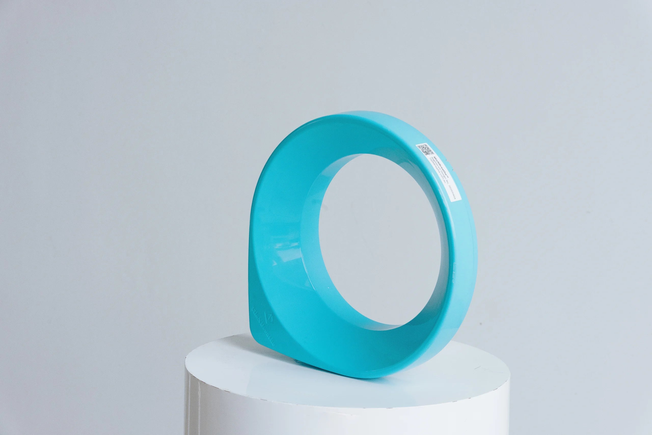 Turquoise circular object on a white pedestal against a light gray background